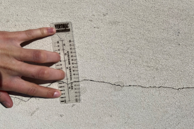 Personne mesurant une fissure sur une façade avec un mètre ruban.